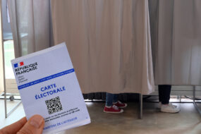 Carte électorale tenue en main devant des isoloirs