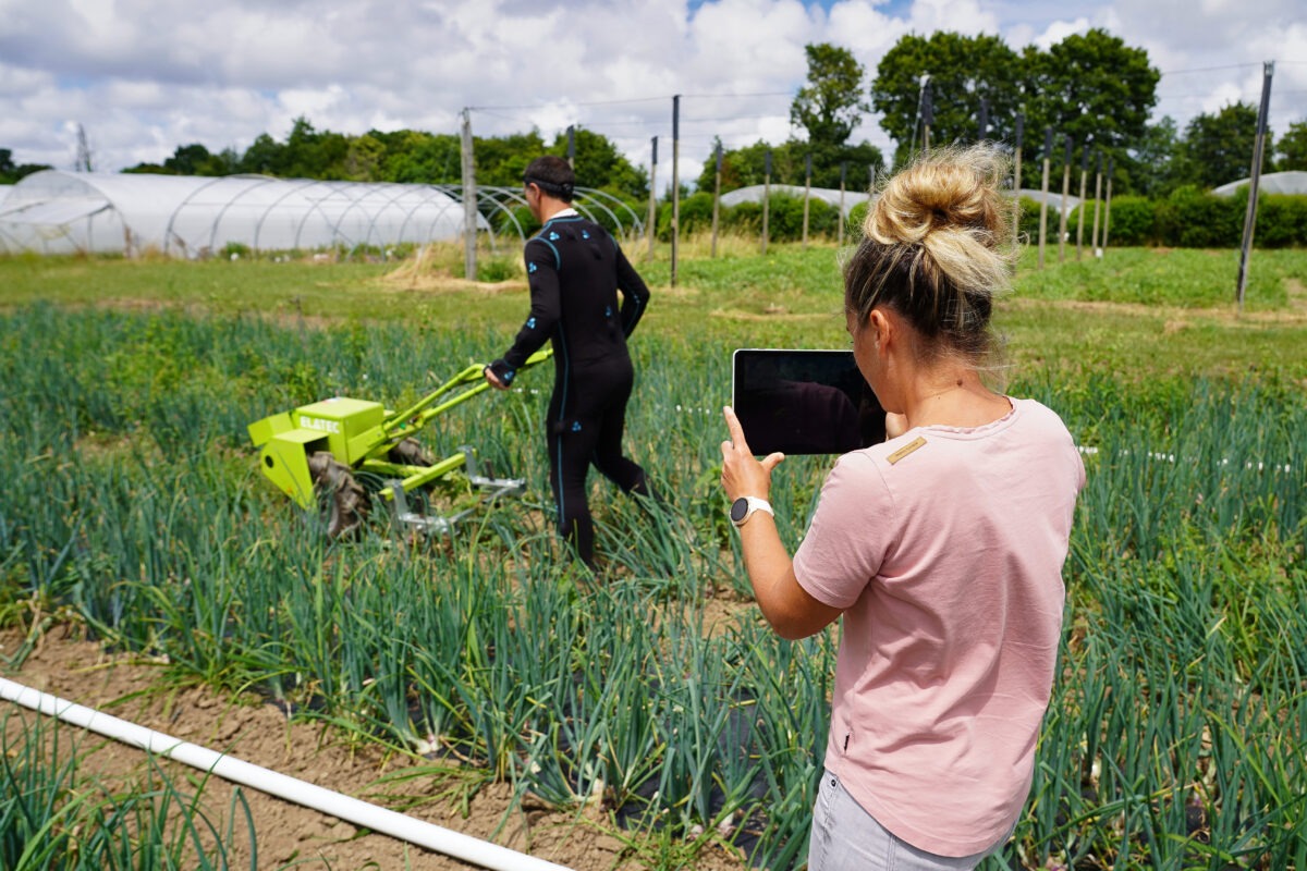 Une femme et un homme dans un champ en train de mesurer des points de tension grâce à une combinaison connectée - Illustration Une diversité de sujets à Auray