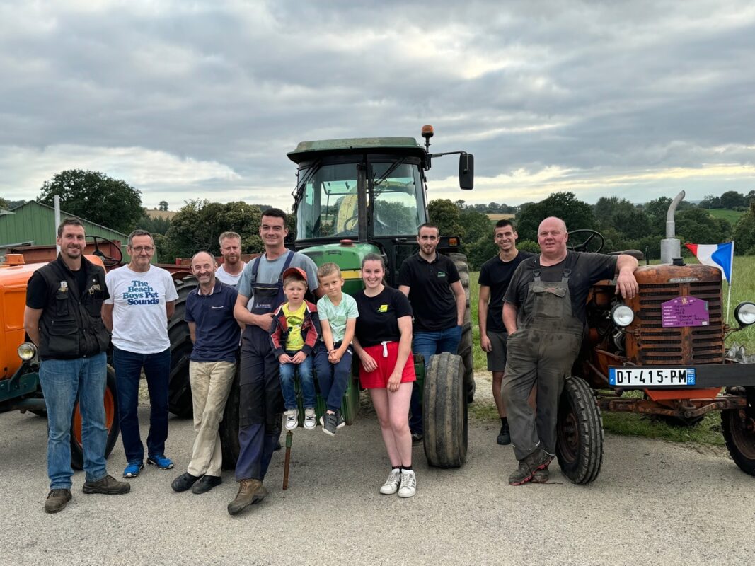 Un groupe d'agriculteurs devant des tracteurs anciens. 