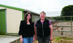 Deux femmes devant un bâtiment de poules pondeuses.