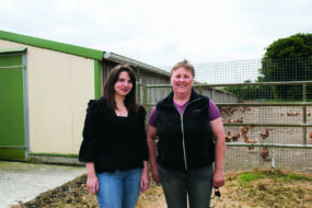 Deux femmes devant un bâtiment de poules pondeuses.