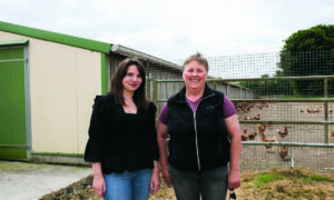 Deux femmes devant un bâtiment de poules pondeuses.