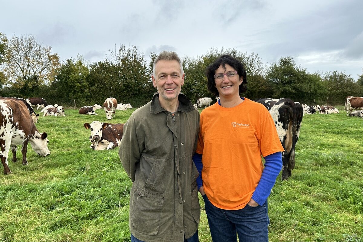 Agriculteur et salariée de l'idèle dans une prairie avec des vaches Normandes - Illustration « Pas de performance économique  sans robustesse écologique »