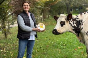 Estelle Viel dans un champ avec un fromage au lait cru et une vache