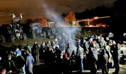 Des agriculteurs manifestant au bord d'un rond-point où sont garés des tracteurs.