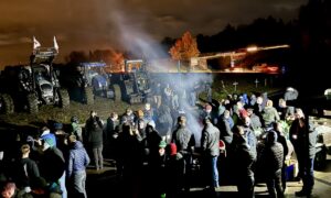 Des agriculteurs manifestant au bord d'un rond-point où sont garés des tracteurs.