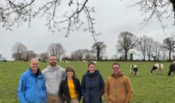 Trois hommes et deux femmes devant un eprairie avec des vaches laitières au pâturage