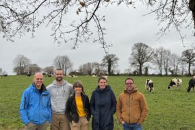 Trois hommes et deux femmes devant un eprairie avec des vaches laitières au pâturage