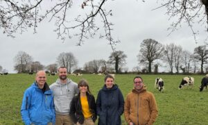 Trois hommes et deux femmes devant un eprairie avec des vaches laitières au pâturage