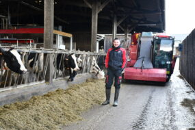 Alexis Robert devant la mélangeuse dans le couloir d'alimentation avec les vaches