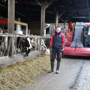 Alexis Robert devant la mélangeuse dans le couloir d'alimentation avec les vaches