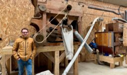 Un paysan pastier devant deux machines anciennes en bois permettant de travailler le grain.