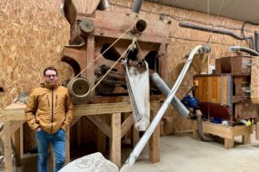 Un paysan pastier devant deux machines anciennes en bois permettant de travailler le grain.