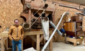 Un paysan pastier devant deux machines anciennes en bois permettant de travailler le grain.