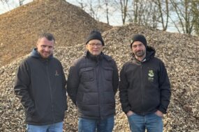 Trois hommes devant un tas de bois déchiqueté.